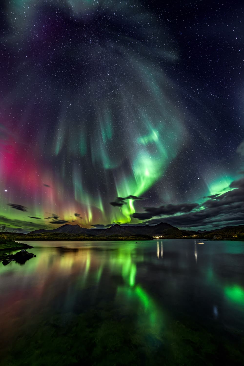 Multicoloured aurora corona bursting over a fjord, mirrored in the water
