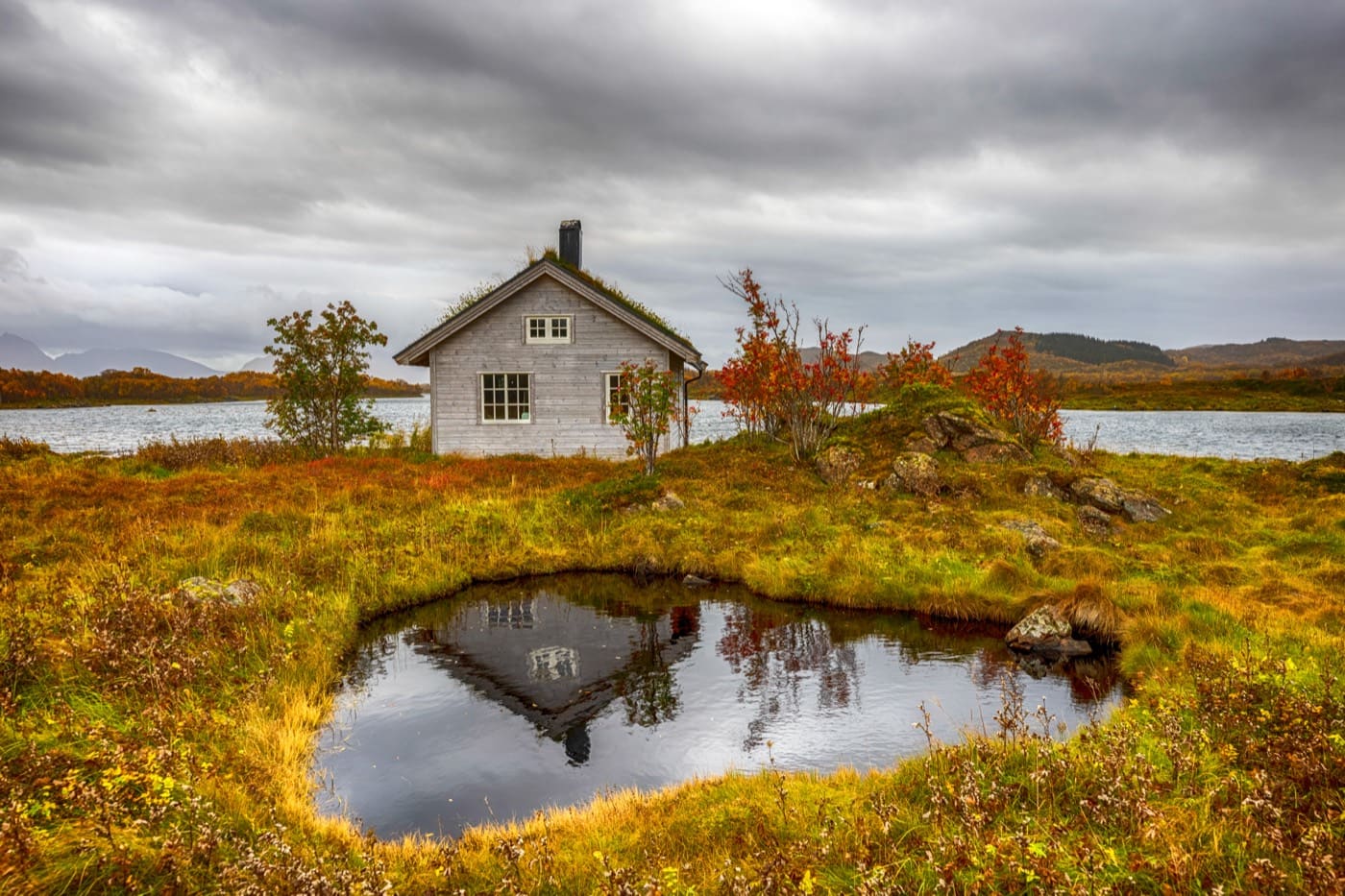 Small cabin beside a tarn in red and gold autumn moorland under heavy clouds